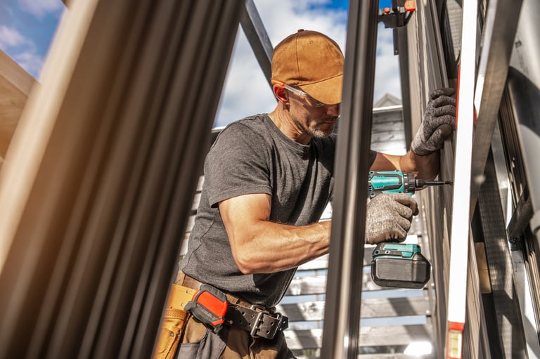 A construction worker focuses on installing lamella wall panels using a power tool while wearing protective gear in bright daylight, showcasing skill and dedication.