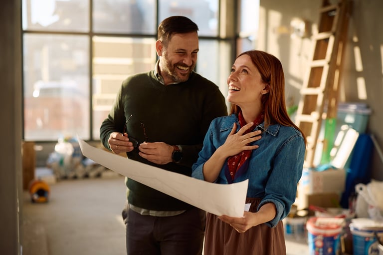 Happy couple laughing while examining blueprints during home remodeling process.